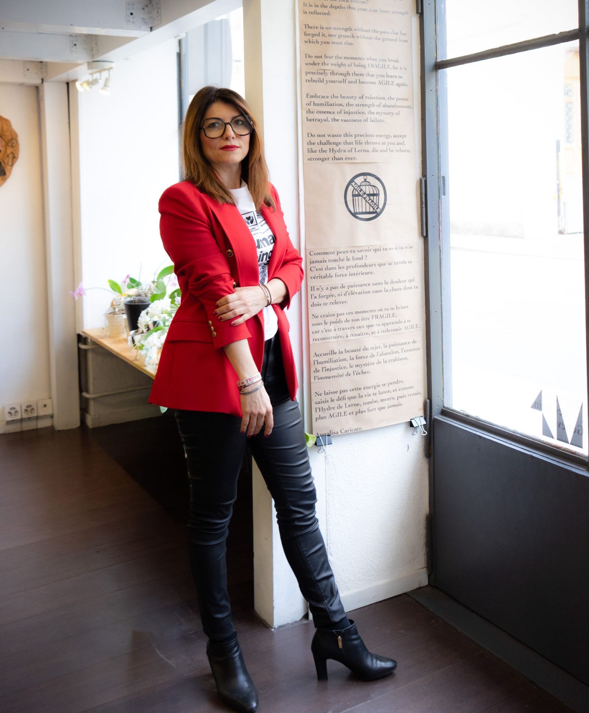 Annalisa Caricato in a red jacket and glasses, standing in the studio beside her manifesto printed on paper.