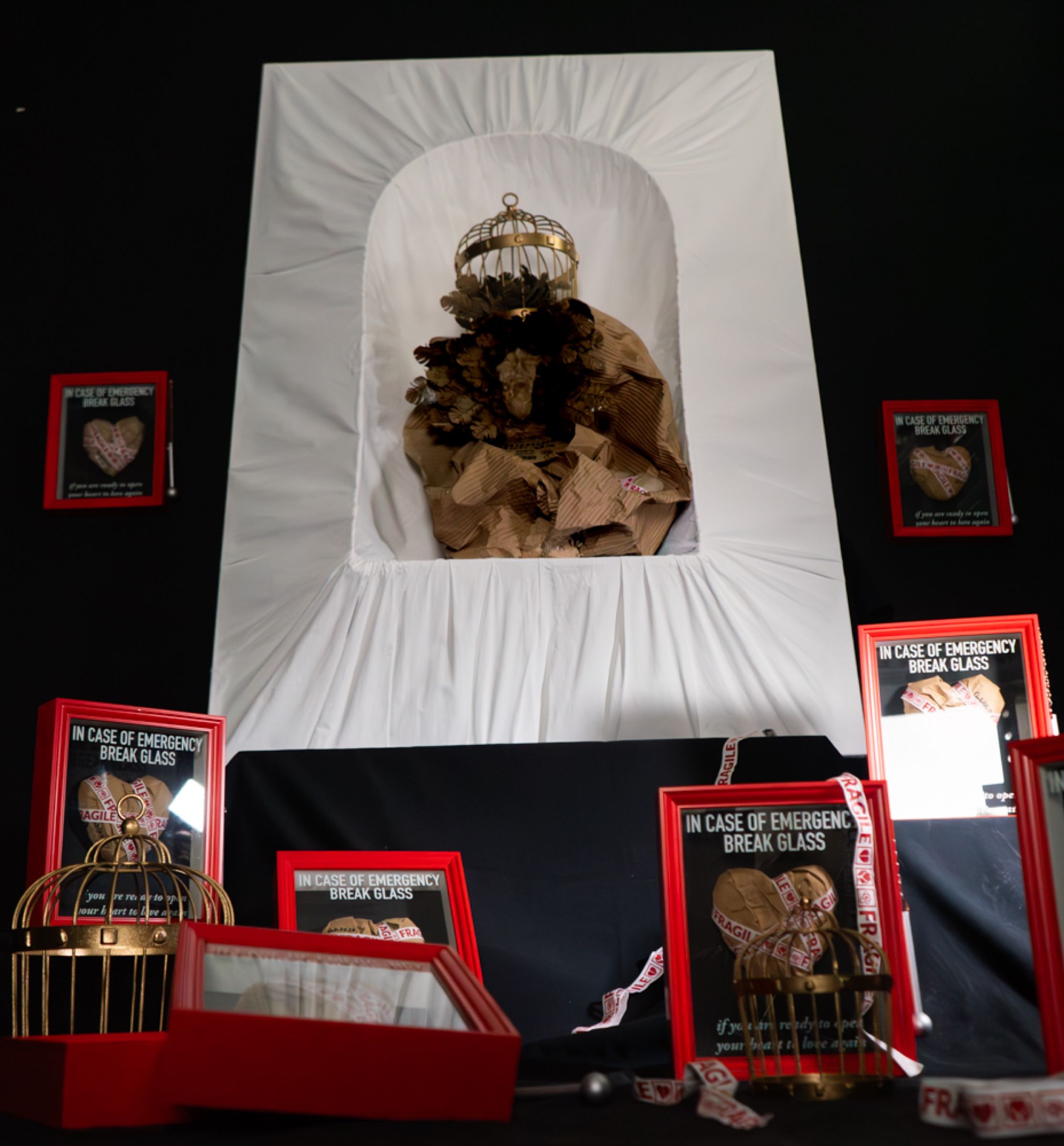 A paper Madonna in a white niche, with red frames and paper hearts at her feet.